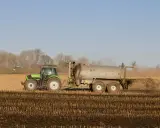 Zielony traktor z przyczepą rozprowadza obornik bydlęcy na polu.