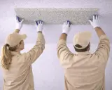 Dwie osoby w beżowych uniformach i czapkach montują panel sufitowy. To praktyczny sposób, jak wyrównać sufit.