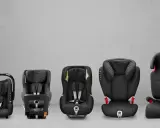 Five black car seats of varying sizes are displayed in a row against a grey concrete background.