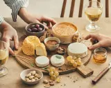 Un tableau accord vin et fromage avec divers fromages, olives, noix, raisins, pistaches et miel.