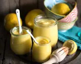 Drei Gläser mit cremigem Lemon Curd, Löffel und frische Zitronen. Perfekt für ein einfaches Lemon Curd Rezept.