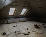 Chantier sous les combles : pose du frein vapeur, deux fenêtres de toit, radiateurs et outils sur le plancher en bois.