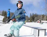 Ungdom åker snowboard i backen, redo för nästa trick. Solen skiner och snön ligger vit.
