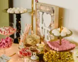 Un candy bar lleno de dulces rosas y blancos, con un letrero de "LOVE" y luces cálidas.