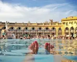 Fötter sticker upp ur vattnet i ett soligt budapest spa. Människor badar och njuter av den vackra arkitekturen.