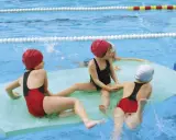 Niños divirtiéndose con juegos en la piscina, sentados en flotadores y chapoteando.