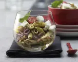 Ein köstlicher Nudel Pesto Salat mit Mozzarella, Pinienkernen, Rosinen und roten Zwiebeln in einem Glas serviert.