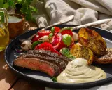 Skivad flapsteak marinad med rostade potatishalvor, tomatsallad och krämig sås.