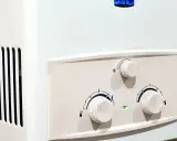 Ein weißer Gas-Durchlauferhitzer mit drei Reglern und einer grünen Kontrollleuchte.