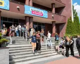 Grupa młodych ludzi schodzi po schodach przed budynkiem, gdzie wisi baner "Spotkajmy się w Kortowie!". To idealne miejsce na rozpoczęcie studiów w Olsztynie.
