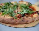 Pyszne ciasto na pizzę z rukolą, oliwkami i papryką, podane na drewnianej desce.