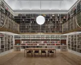 A grand library with towering bookshelves, a central reading table, and a modern globe light. This space feels like a capital photography center for learning.