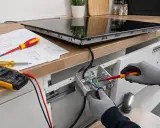 Instalator podłącza płytę indukcyjną 3-fazową, używając śrubokręta i instrukcji. Obok leży multimetr.
