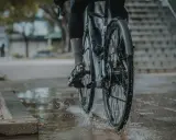 Rowerzysta w deszczu, koła rozpryskują wodę. Montaż błotnika rowerowego zapewnia suchą jazdę.