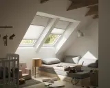 Habitación infantil con dos ventanas de tejado equipadas con cortinas para Velux caseras, cama baja, cuna y juguetes.