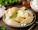 Pyszne pierogi z serem, udekorowane miętą i posypane białym serem. Obok słoiczek miodu i miseczka z serem.
