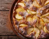 Un délicieux clafoutis aux pommes, saupoudré de sucre glace, repose sur un plateau en bois rustique.