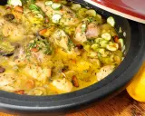 Tajín de pollo con calabacín, aceitunas y almendras, servido en una cazuela de barro, con limones frescos al lado.