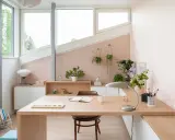 Une petite chambre avec bureau, lumineuse et décorée de plantes. Le bureau en bois clair est prêt pour le travail ou la lecture.