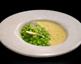 Un plato de guisantes de lágrima frescos con una cremosa sopa amarilla y una fina lámina de champiñón.