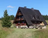 Drewniana bacówka na Krawcowym Wierchu, otoczona zielenią i lasem. Obok stoi stary traktor.