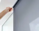 Ręka reguluje mechanizm rolety w kasecie. Dowiedz się, jak naprawić roletę w kasecie, gdy sznurek się zerwie.