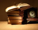 Un libro aperto con occhiali da lettura, una pila di antichi volumi e un orologio da tavolo. Un invito a leggere Catullo: "dammi mille baci".