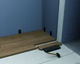 Instalación de suelo laminado. Se ven piezas de madera, un mazo y soportes para el rodapié que es la pieza final.