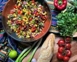 Bunter mexikanischer Salat mit Mais, Bohnen und Gemüse in einer Schüssel, daneben Baguette, Tomaten und Kräuter.