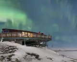 Två personer njuter av norrskenet från en aurora sky station i snöig fjällmiljö.