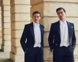 Two men in formal attire, a white tie event, stand by a stone colonnade.