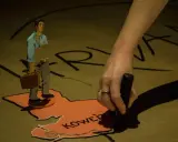 Une main appose un tampon sur la carte du Koweït, où un homme en carton, valise à la main, semble prêt à partir. Tout part à volo.