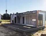 Budowa domu na zgłoszenie postępuje. Dźwig podnosi moduł, a pracownicy w kamizelkach nadzorują montaż. Warunki zabudowy sprzyjają szybkiemu postawieniu konstrukcji.