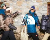 Cztery osoby w kurtkach The North Face, z plecakami i torbami, na tle kamiennej ściany. Jak rozpoznać podróbkę? Sprawdź detale!