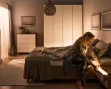 Kobieta szuka czegoś w szufladzie nocnej, która jest podświetlana. Idealna lampa do sypialni powinna tworzyć taki przytulny nastrój.