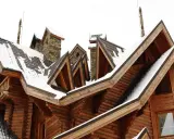 Drewniany dom z licznymi lukarny rodzaje, pokryty śniegiem. Dachówki i kamienne kominy tworzą malowniczy krajobraz.