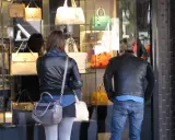 Coppia osserva vetrina di borse Benetton a Riccione. Lei con giacca in pelle, lui con giubbotto.