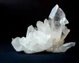 Un grappolo di cristalli di quarzo trasparenti e luminosi su sfondo scuro. Questo è un esempio di che cos'è il quarzo, un minerale comune e versatile.