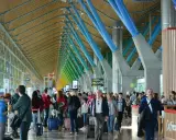 Ludzie z bagażami w nowoczesnym terminalu, jednym z wielu lotnisk w Europie, podziwiają architekturę z kolorowymi podporami.