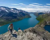 Vandrare klättrar på en bergskam med en turkos sjö nedanför. Besseggen svårighetsgrad är utmanande men belönande.