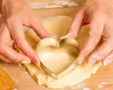 Manos cortan masa con un cortador en forma de corazón, parte de una receta de galletas.