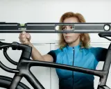 Kobieta z poziomicą sprawdza, jak dopasować rower, mierząc wysokość siodełka i kierownicy.