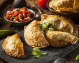 Gyllene argentinska empanadas recept på en svart stenplatta, serverade med färsk salsa och tortillachips.