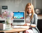 Uśmiechnięta kobieta prezentuje laptop z napisem "Z nami pokochasz język szwedzki!". Idealna dla studentów filologii szwedzkiej w Warszawie.