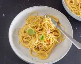 Ein Teller mit cremiger Spaghetti Carbonara, garniert mit Basilikum und Speckstückchen.