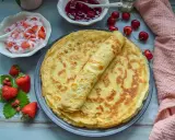 Omas Pfannkuchen-Rezept: goldbraune Pfannkuchen auf einem Teller, dazu Erdbeerquark, Kirschmarmelade und frische Erdbeeren.