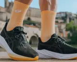 Biegacz w pomarańczowych skarpetkach z logo Asics i ciemnych butach tej firmy, gotowy do podboju miasta.