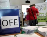 Na biurku leży segregator z napisem OFE. Ludzie stoją przy tablicy informacyjnej ZUS, pytając, czy można wypłacić pieniądze z OFE.