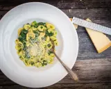 Orecchiette mit Cime di Rapa, frisch geriebenem Parmesan und einem Löffel auf einem Holztisch.