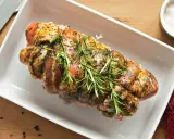 Un rôti de porc cru, assaisonné et garni de romarin frais, prêt à être cuit dans un plat blanc.